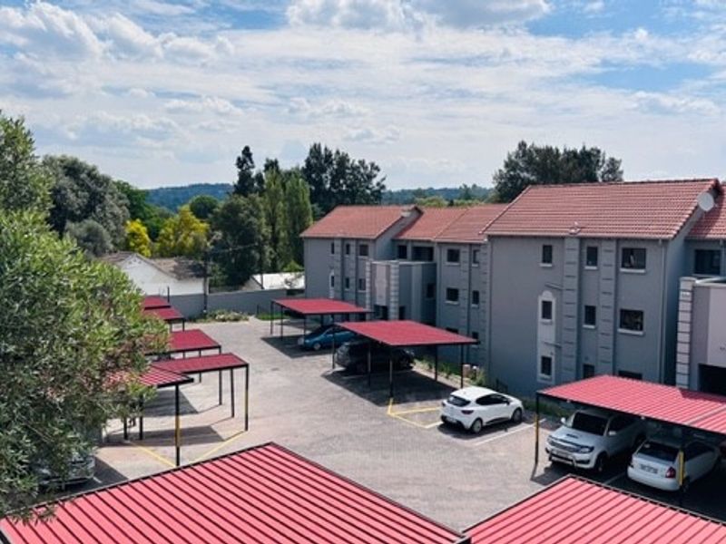 An elevated view of an apartment complex featuring multiple covered parking bays, paved driveway areas, and multi-story residential buildings with tiled roofs.