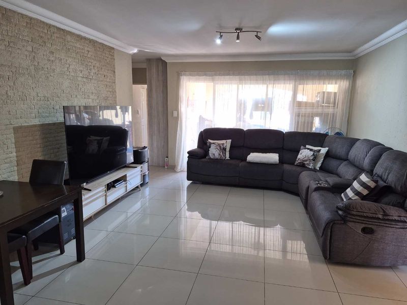Spacious living room featuring polished porcelain floor tiles, a textured stone feature wall, and ceiling coving, providing a modern and comfortable living space.