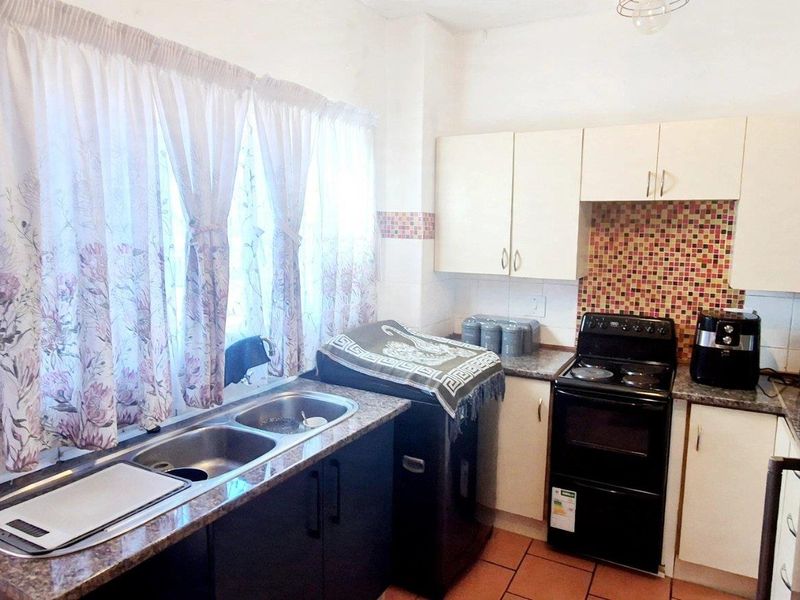 A functional kitchen featuring granite countertops, mosaic tile backsplash, double bowl sink, and built-in cabinetry with a freestanding stove.
