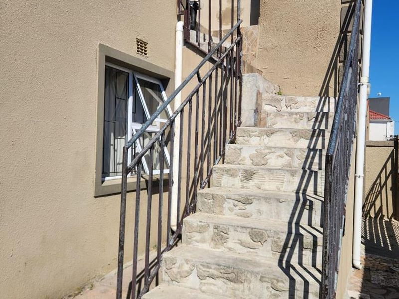 Exterior rear staircase featuring stone steps and metal handrails leading to an upper level entrance, showing signs of significant wear and weathering.