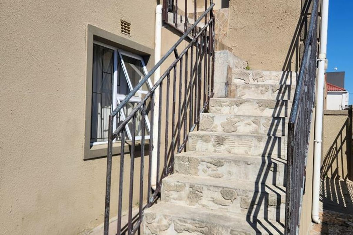Exterior rear staircase featuring stone steps and metal handrails leading to an upper level entrance, showing signs of significant wear and weathering.
