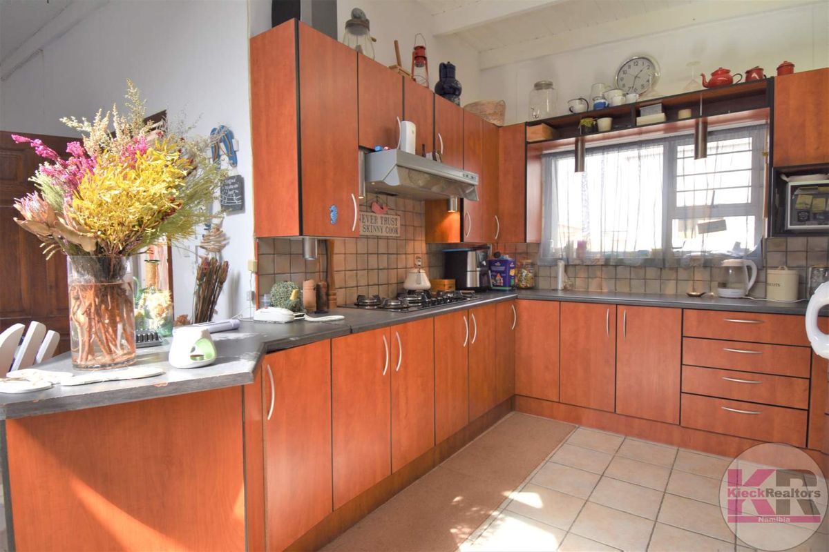 A functional kitchen featuring wood-look cabinetry, tiled splashbacks, a built-in gas hob, and an extractor fan, offering a practical layout for daily meal preparation.