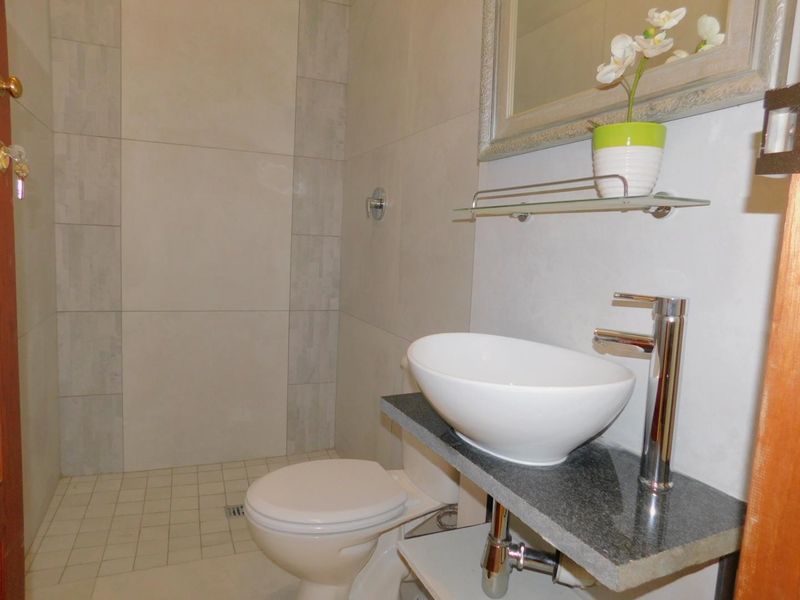 A modern bathroom featuring a vessel sink on a stone vanity, a toilet, and a tiled walk-in shower area.