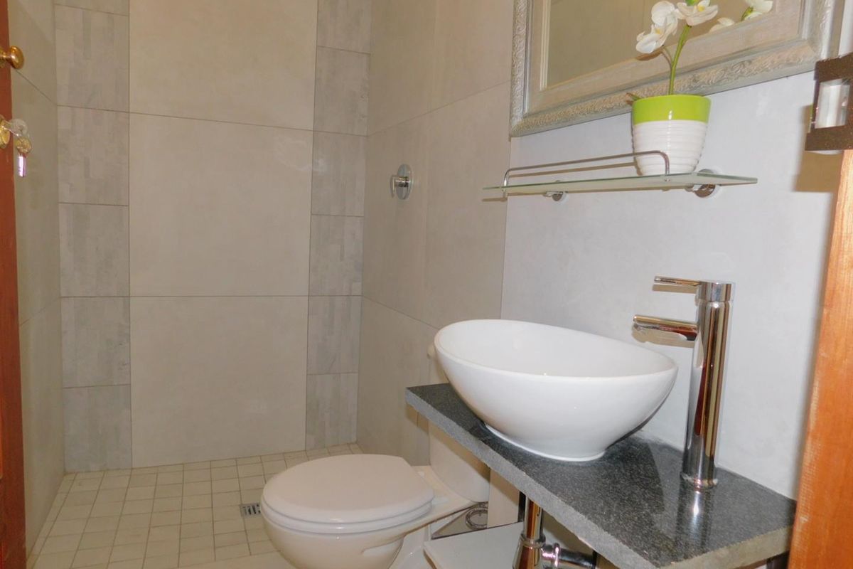 A modern bathroom featuring a vessel sink on a stone vanity, a toilet, and a tiled walk-in shower area.