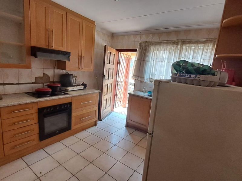 A functional kitchen featuring wooden cabinetry, built-in oven, extractor fan, and tiled flooring, with direct access to the exterior.