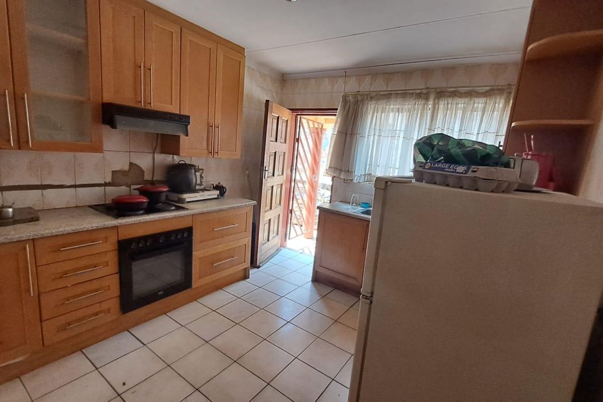 A functional kitchen featuring wooden cabinetry, built-in oven, extractor fan, and tiled flooring, with direct access to the exterior.