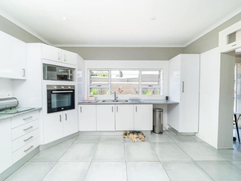 A bright, modern kitchen featuring white cabinetry, built-in oven and microwave, double sink, and neutral tiled flooring.