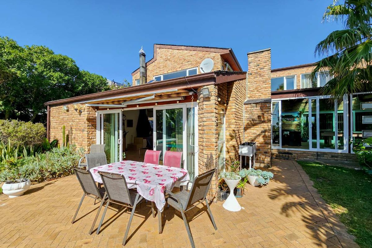 Rear view of the house featuring a brick facade, paved patio area, and large sliding glass doors providing seamless indoor-outdoor flow.
