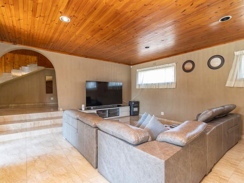 Spacious living room featuring a warm timber-paneled ceiling, tiled flooring, and an arched transition leading to an elevated area.