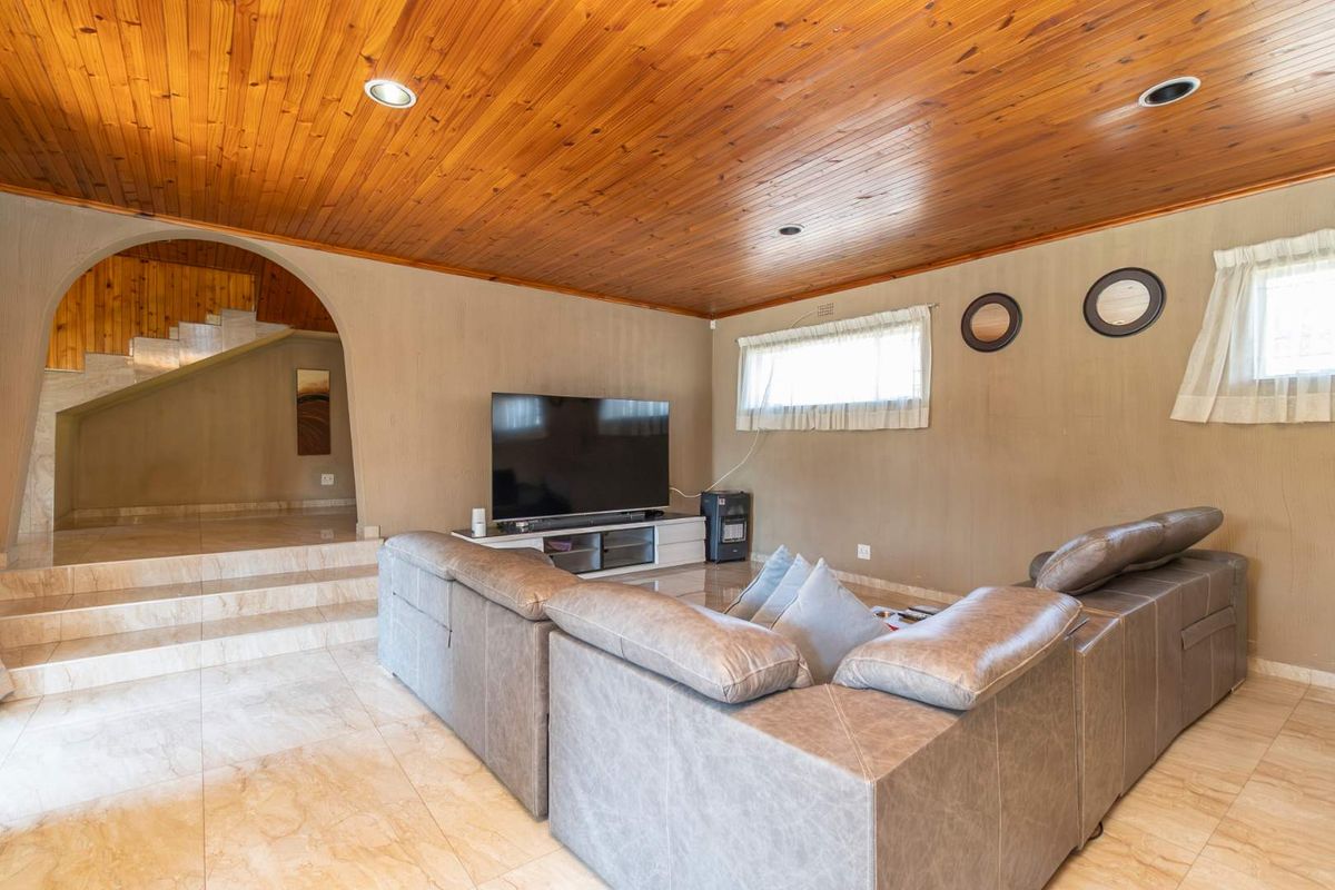 Spacious living room featuring a warm timber-paneled ceiling, tiled flooring, and an arched transition leading to an elevated area.
