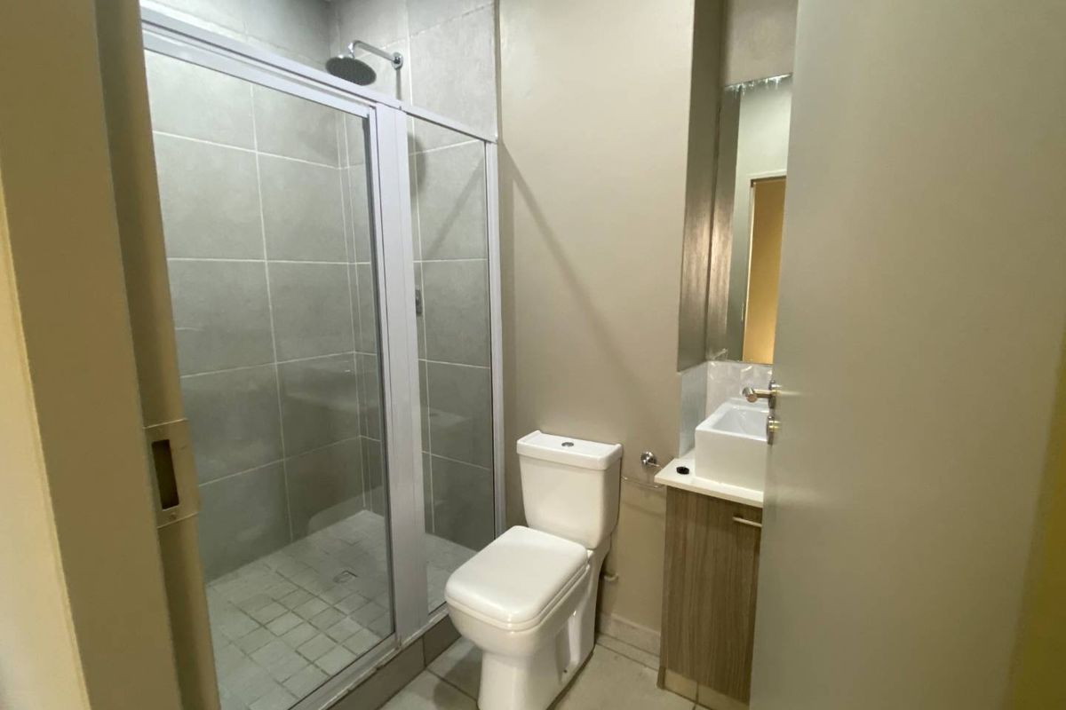 A clean and functional bathroom featuring a glass-enclosed shower, modern toilet, and a vanity unit with a basin and wall-mounted mirror.