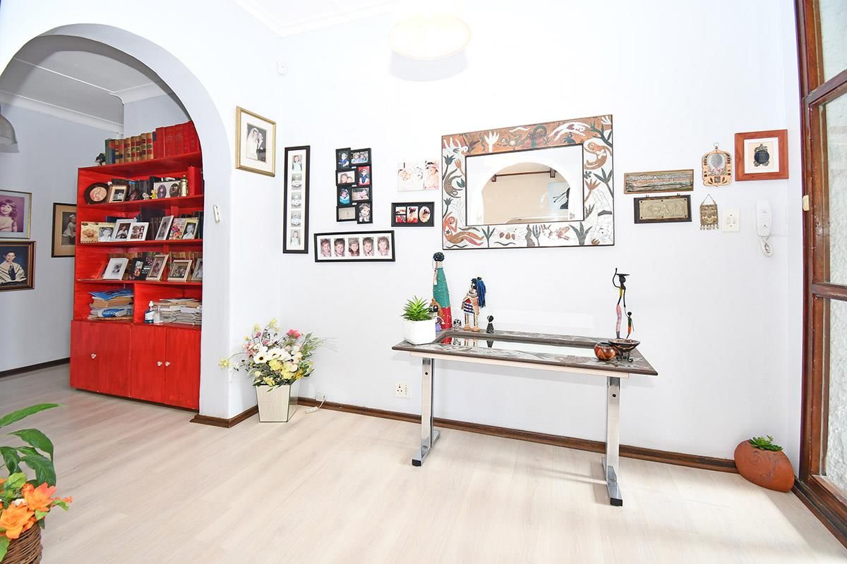 A bright living area featuring light wood-look flooring, a decorative arched entryway, and a built-in red display shelving unit.