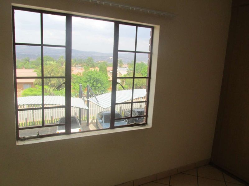 An empty bedroom featuring tiled flooring, a built-in cupboard, and a steel-framed window with views of the complex parking area.
