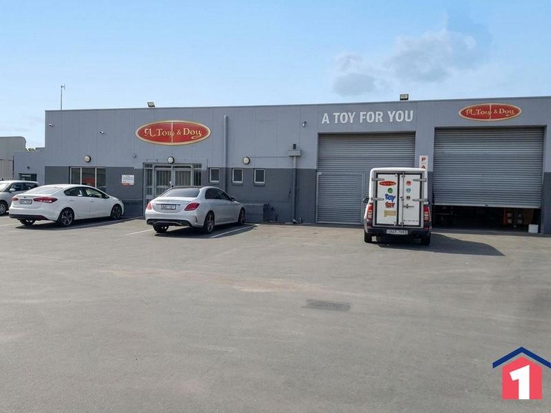 Front elevation of an industrial property featuring roller shutter doors, paved parking area, and prominent commercial signage.