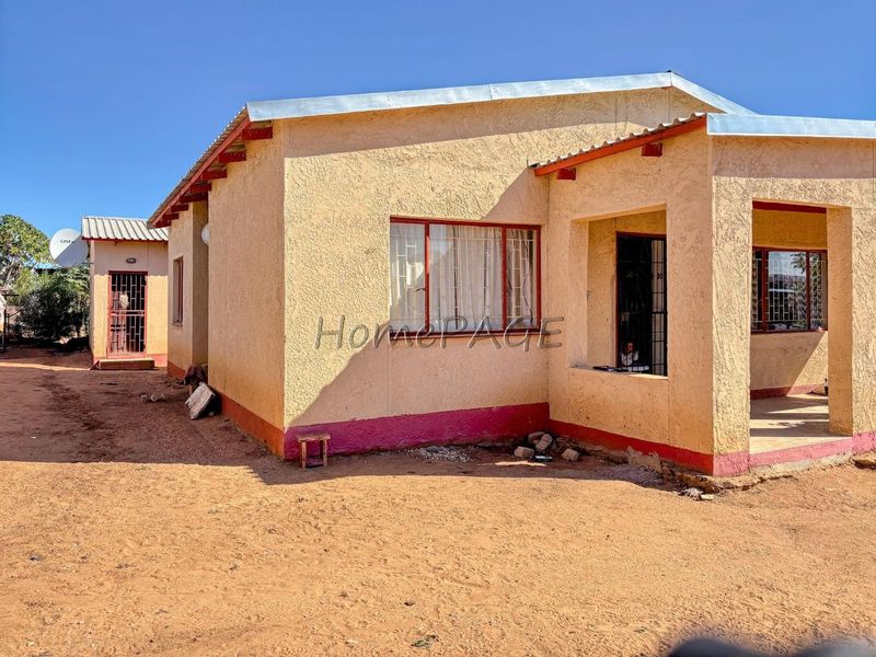 Front view of a single-story residential house featuring plastered walls, a corrugated metal roof, and security bars on windows and doors.