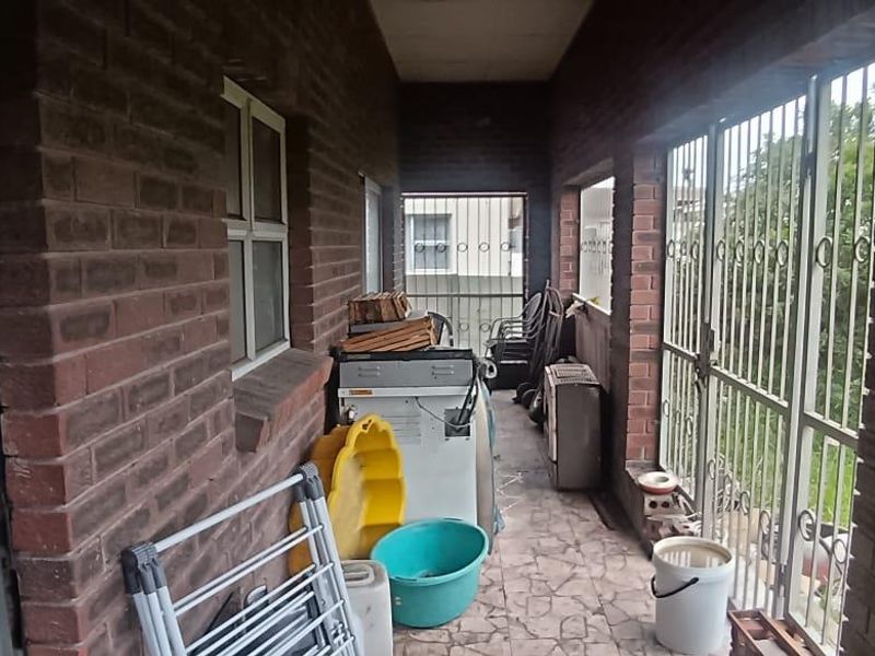 A covered outdoor patio area featuring exposed brick walls, tiled flooring, and secure metal gates, providing a functional transition space.