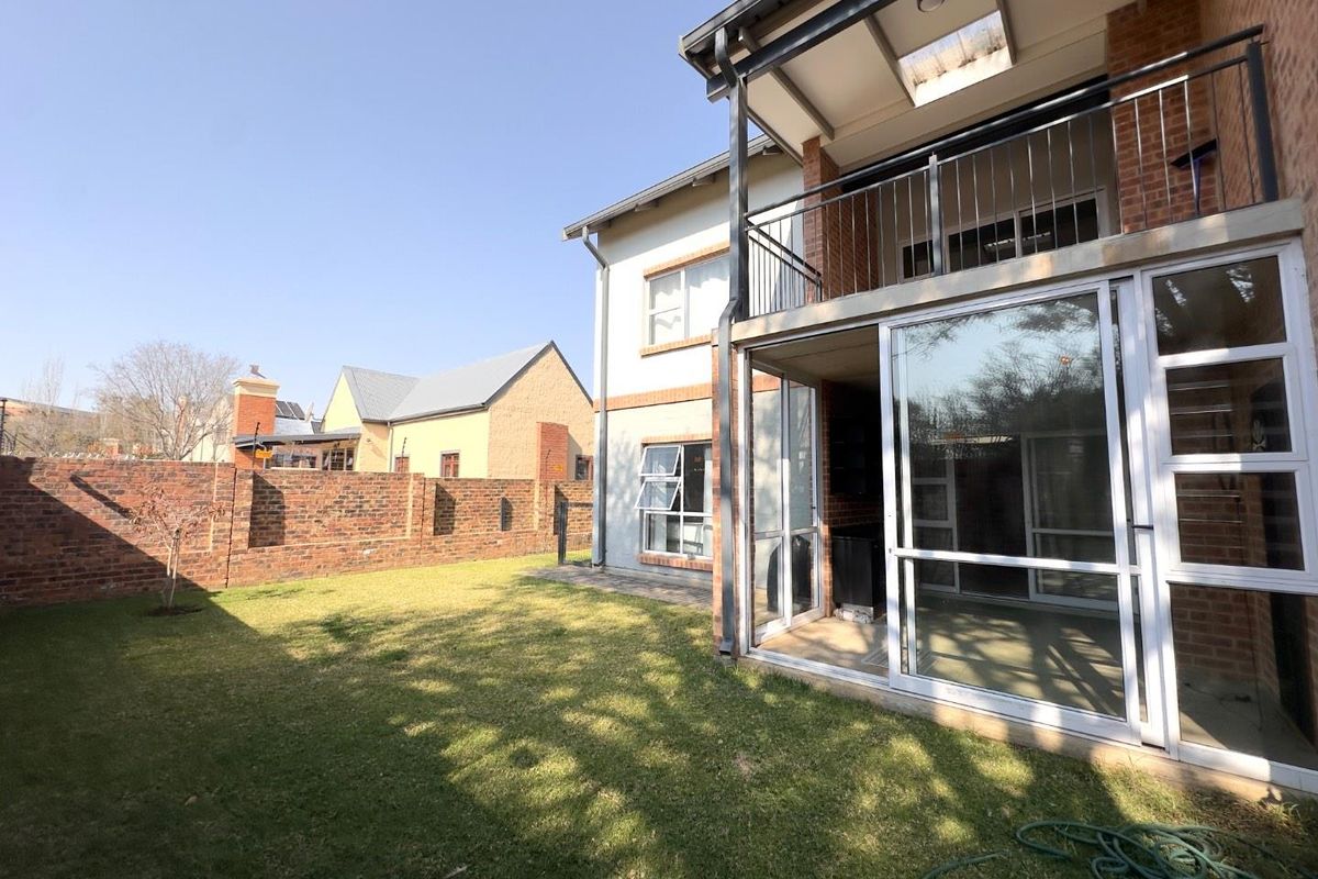 Rear view of the townhouse featuring a private garden, a covered ground-floor patio, and an upper-level balcony with metal railings.