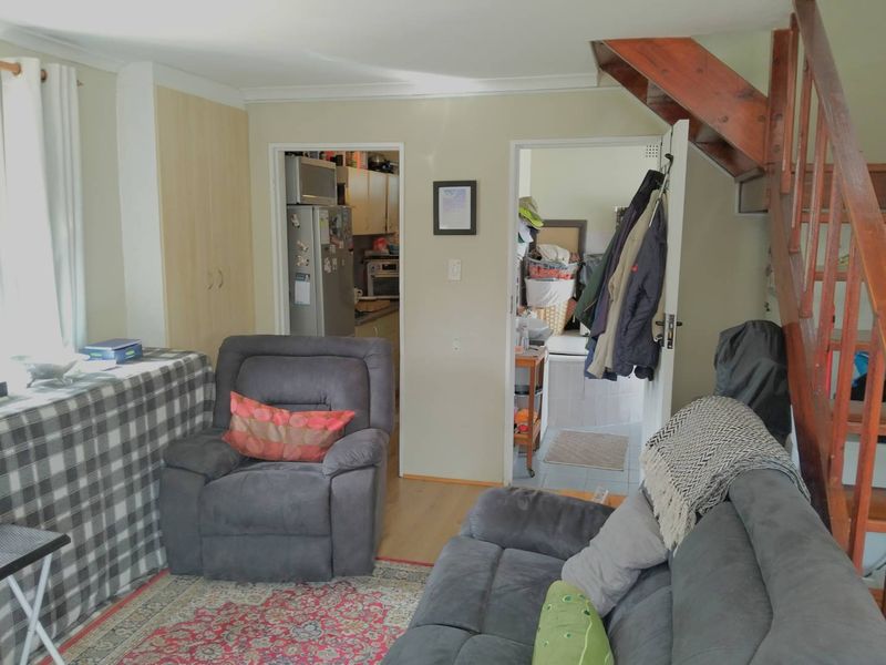 A living room area featuring laminate flooring and a wooden staircase, with direct access to the kitchen and utility spaces.