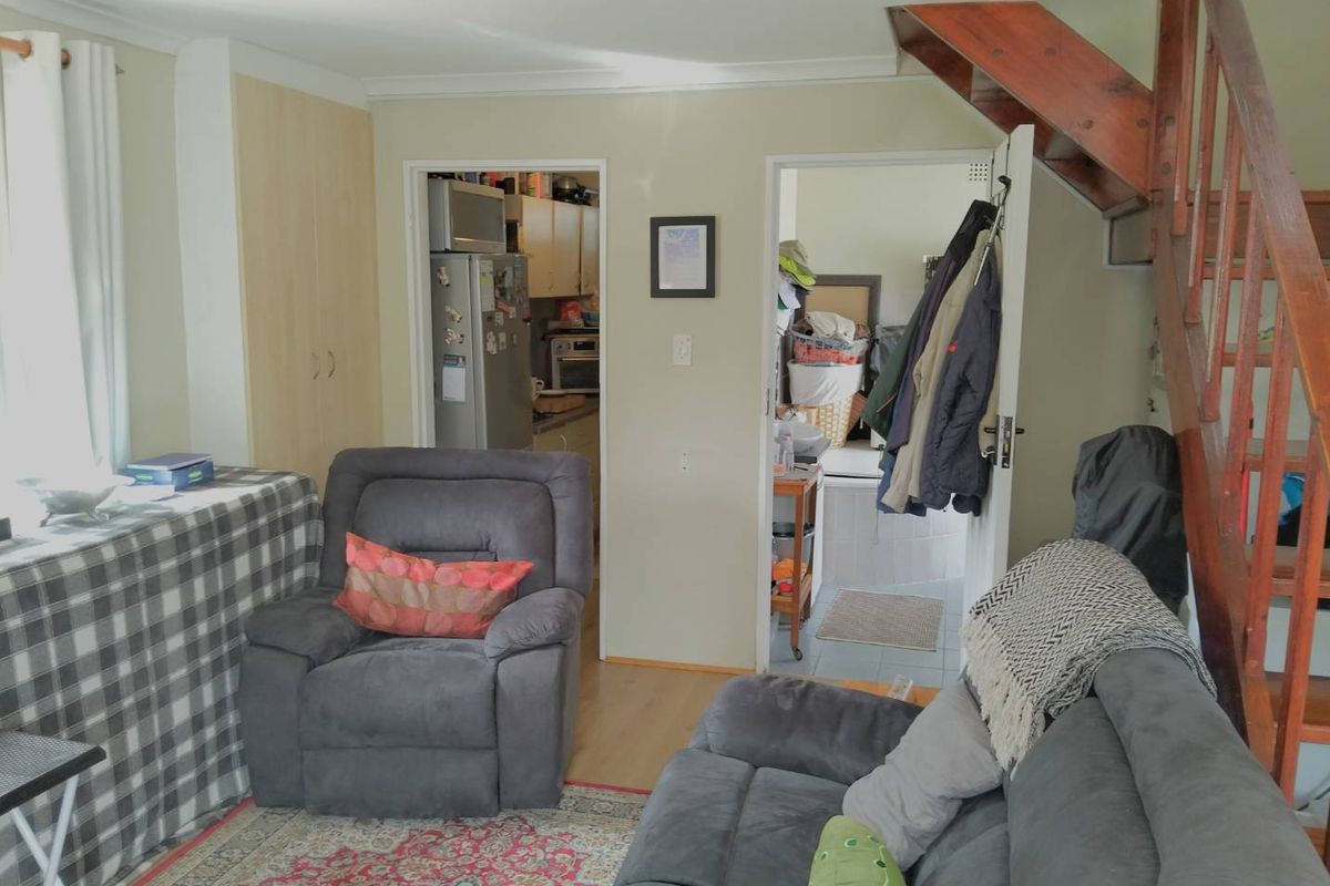 A living room area featuring laminate flooring and a wooden staircase, with direct access to the kitchen and utility spaces.