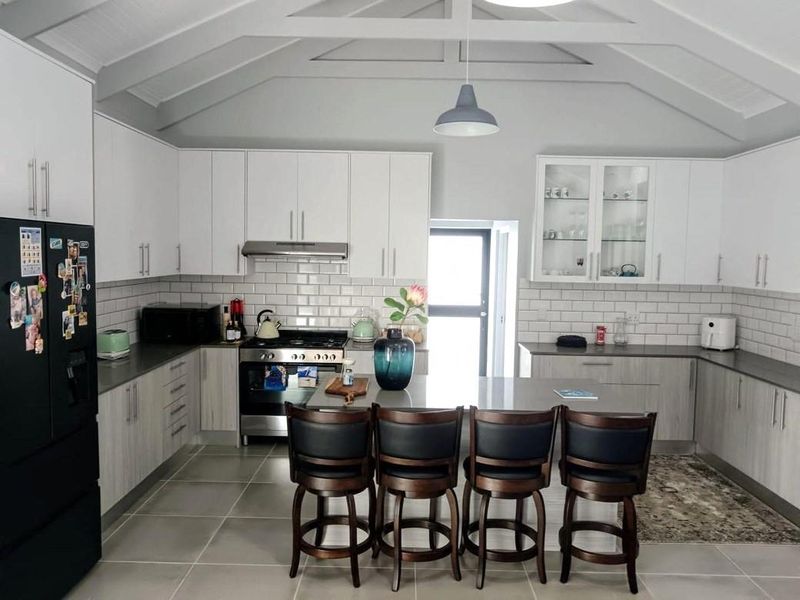 Modern kitchen featuring white cabinetry, stone countertops, subway tile backsplash, and a vaulted ceiling with pendant lighting, creating a bright and functional culinary space.