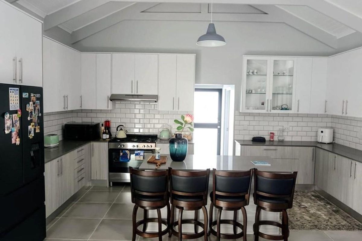 Modern kitchen featuring white cabinetry, stone countertops, subway tile backsplash, and a vaulted ceiling with pendant lighting, creating a bright and functional culinary space.