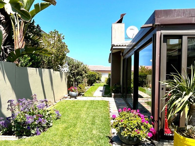 A well-maintained rear garden featuring a manicured lawn, paved pathway, boundary wall, and large sliding glass doors leading into the home.