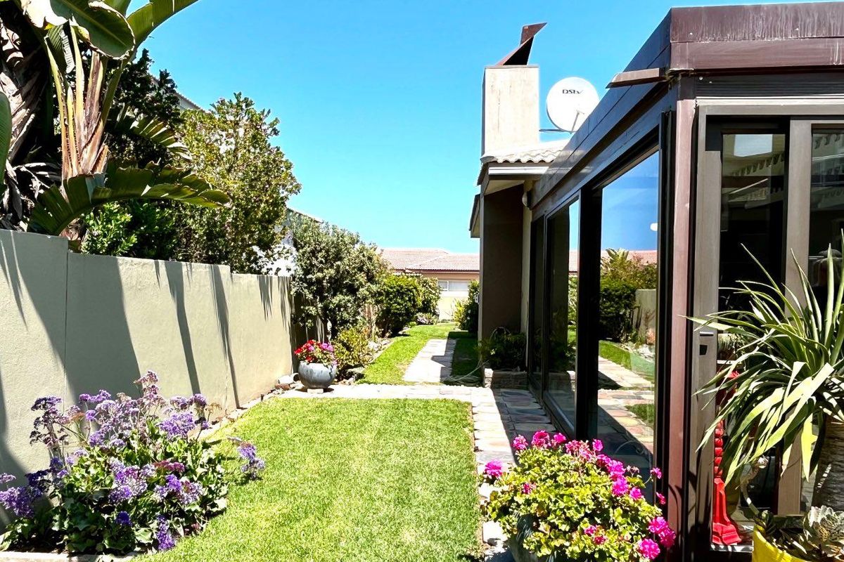 A well-maintained rear garden featuring a manicured lawn, paved pathway, boundary wall, and large sliding glass doors leading into the home.