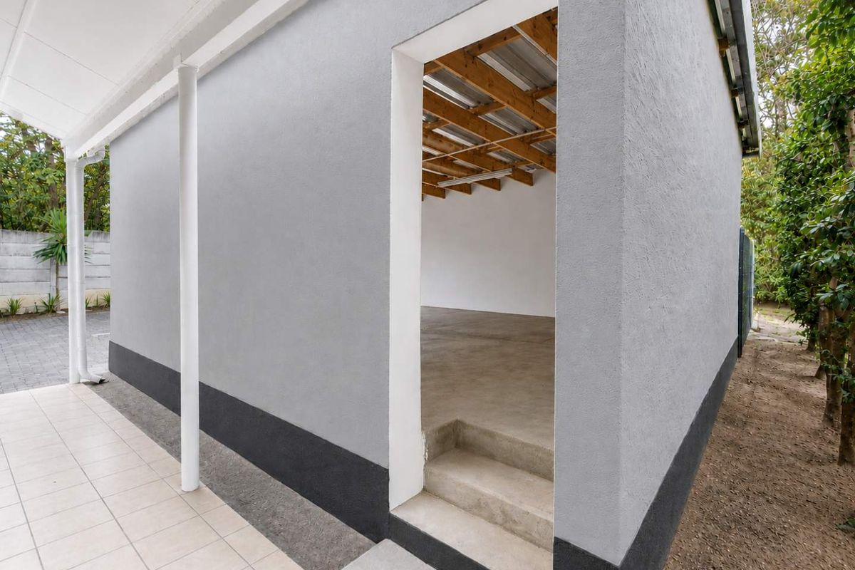 A view of a rear exterior area featuring a tiled patio, painted plaster walls, and an open entrance to an unfinished interior space.