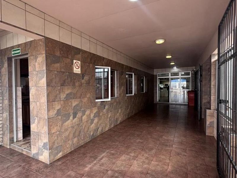 A covered, tiled walkway or corridor featuring stone-look wall tiles, recessed lighting, and secure access points, suitable for commercial or mixed-use property circulation.