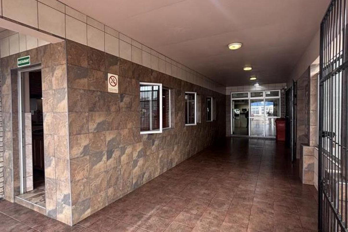 A covered, tiled walkway or corridor featuring stone-look wall tiles, recessed lighting, and secure access points, suitable for commercial or mixed-use property circulation.