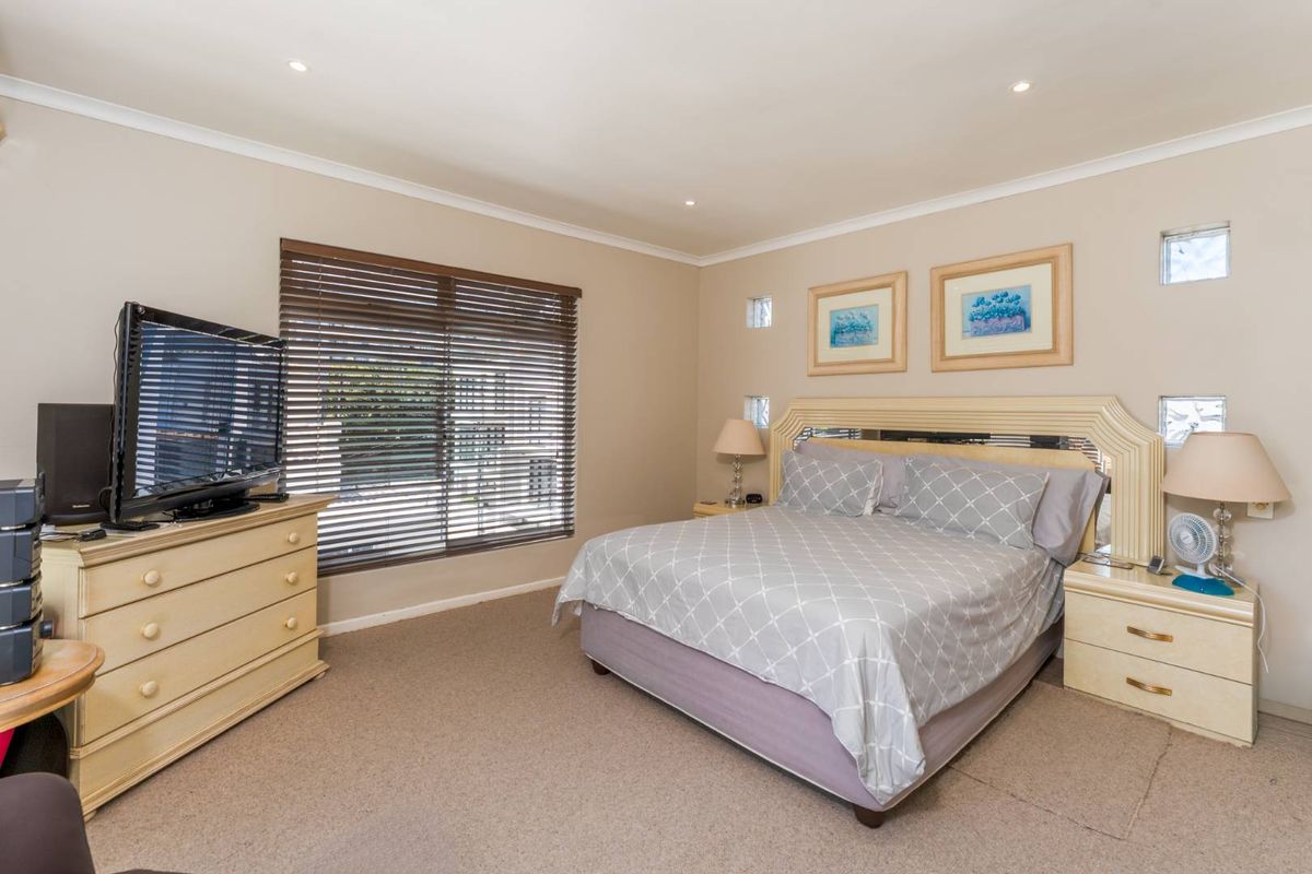 A spacious bedroom featuring neutral wall tones, carpeted flooring, recessed downlighting, and venetian blinds, offering a comfortable and functional living space.