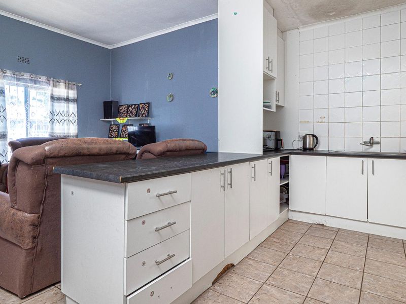 Open plan kitchen and living area featuring white cabinetry, tiled backsplash, and ceramic flooring, showing signs of wear and requiring cosmetic updates.