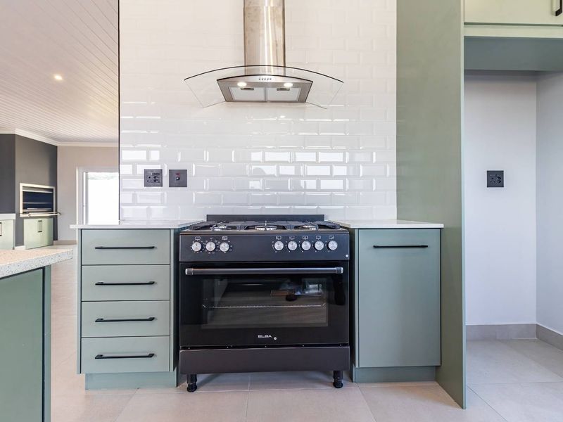 Modern kitchen featuring sage green cabinetry, a black freestanding gas stove with oven, stainless steel extractor fan, and white subway tile backsplash.