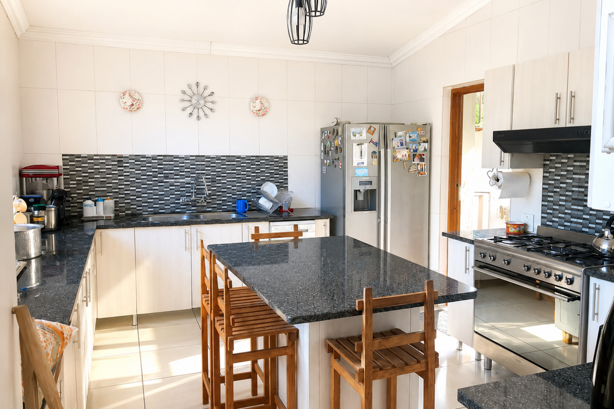 A functional kitchen featuring granite countertops, a central island, gas hob with extractor, and ample built-in cabinetry with a tiled splashback.