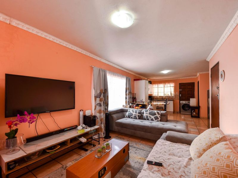 Open-plan living area featuring tiled flooring, decorative ceiling cornices, and an integrated kitchen space with laundry plumbing connections.