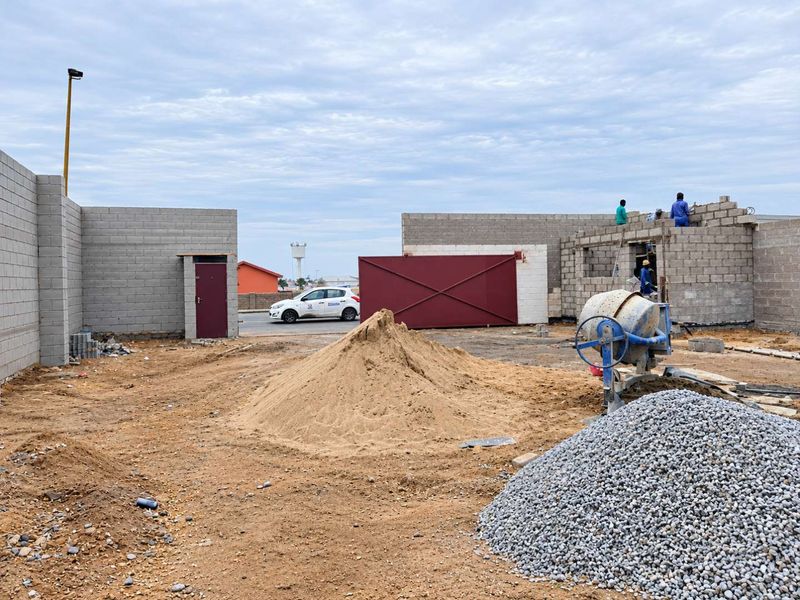 An industrial property under construction featuring concrete block walls, a metal gate, and ongoing site development work.