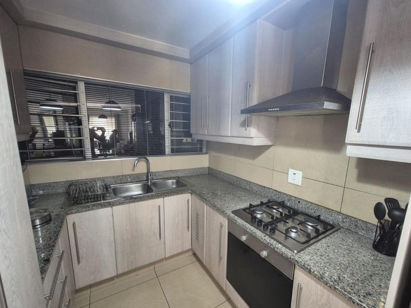 A functional kitchen featuring granite countertops, built-in cabinetry, a gas hob with extractor fan, and a stainless steel double sink.