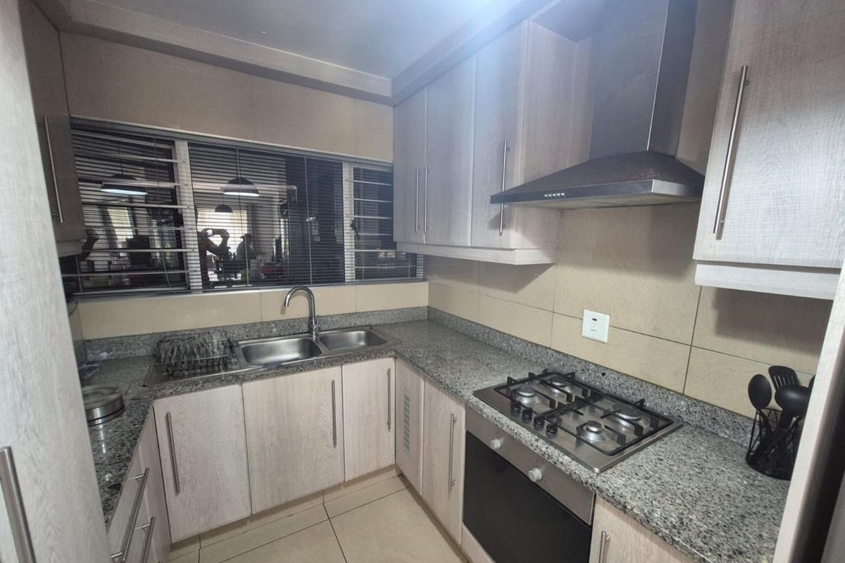 A functional kitchen featuring granite countertops, built-in cabinetry, a gas hob with extractor fan, and a stainless steel double sink.