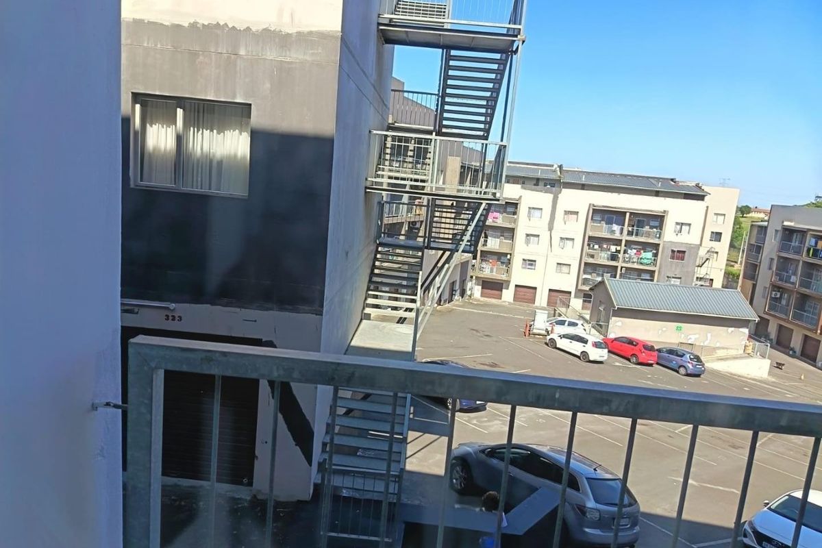 View from a balcony overlooking the rear of the apartment complex, featuring a metal fire escape staircase and parking area.