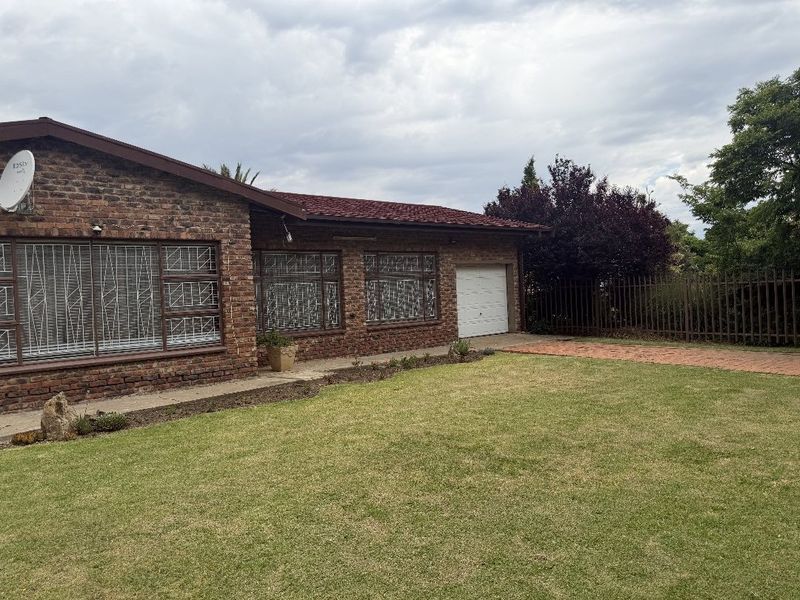 Front view of a face brick house featuring a tiled roof, security bars on windows, a single garage, and a well-maintained lawn.