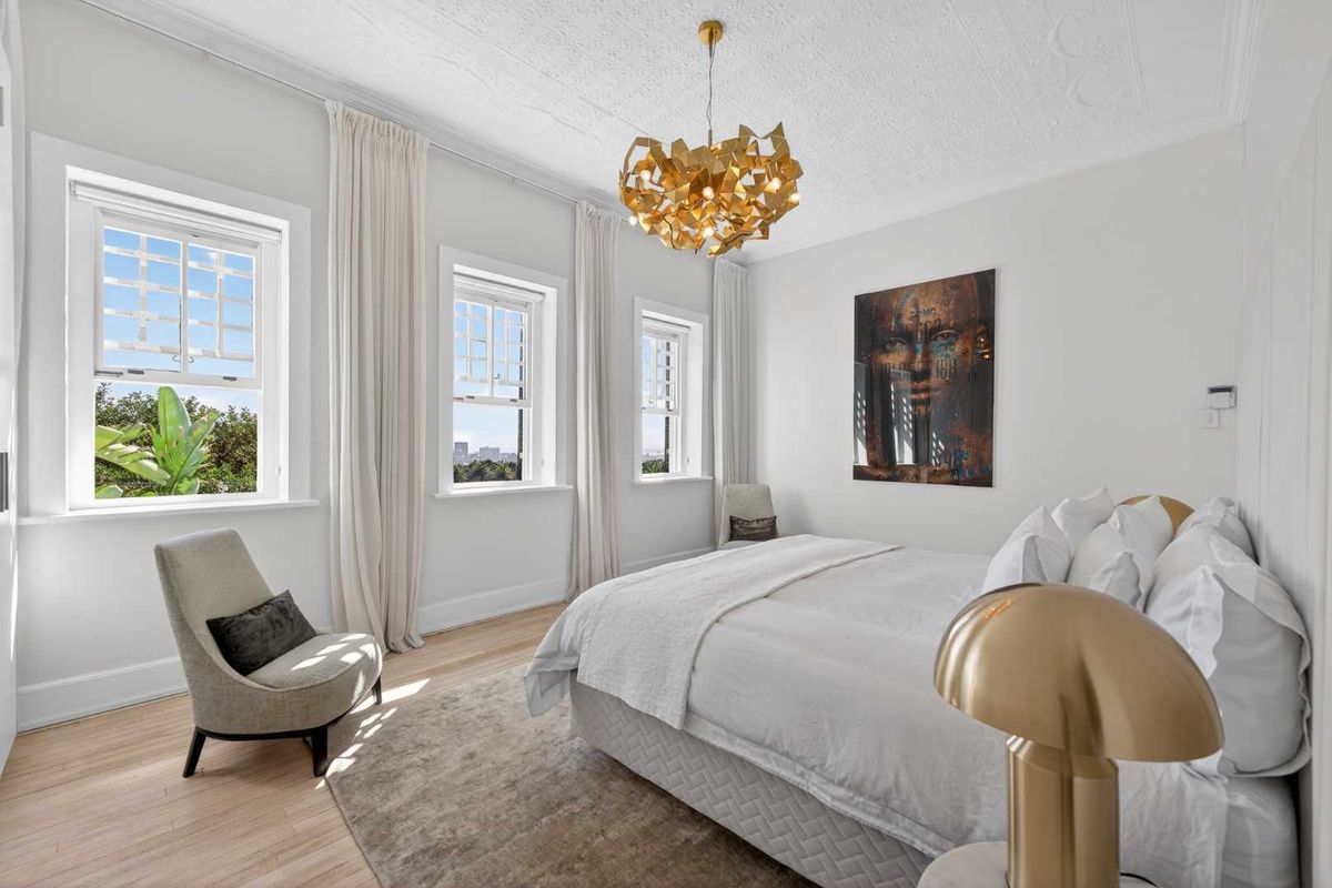 A bright and elegant bedroom featuring timber flooring, classic sash windows, and decorative ceiling detailing, offering a sophisticated and well-maintained living space.
