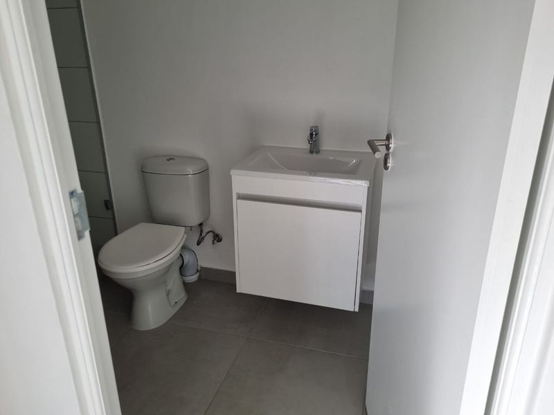 A clean, modern guest bathroom featuring a wall-mounted vanity with a basin and a standard toilet, finished with neutral floor tiles.