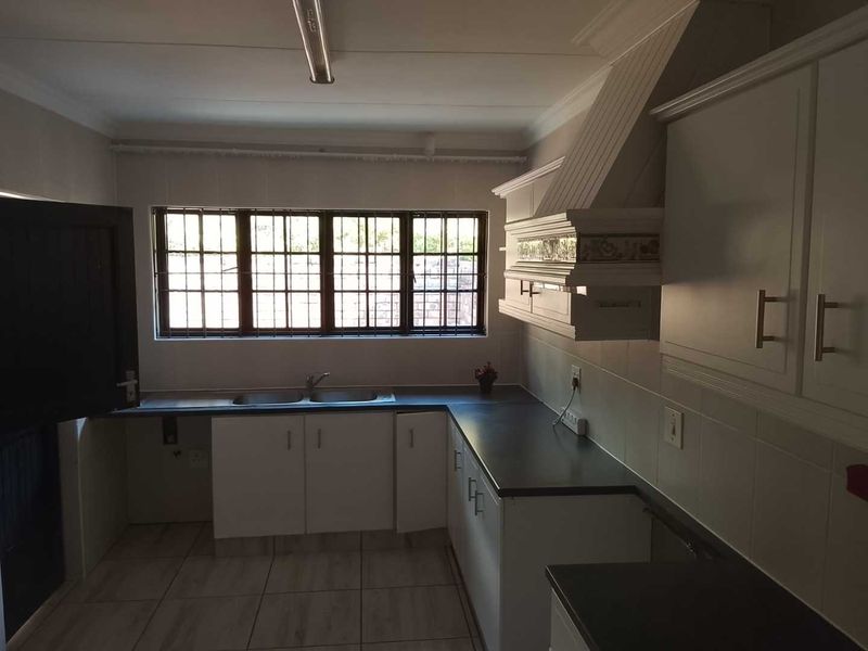 A functional kitchen featuring white cabinetry, a double sink, dark countertops, and tiled flooring, with security bars installed on the window.
