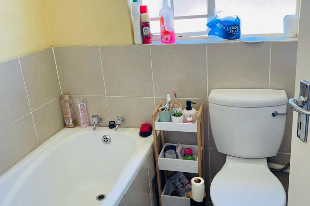 A compact bathroom featuring a standard bathtub, a white ceramic toilet, and tiled wall finishes with a window for natural light.