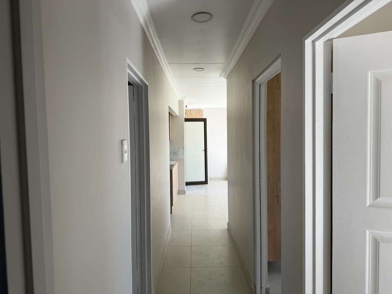 A bright, empty hallway featuring tiled flooring, crown molding, and recessed ceiling lights, providing access to multiple rooms within the townhouse.