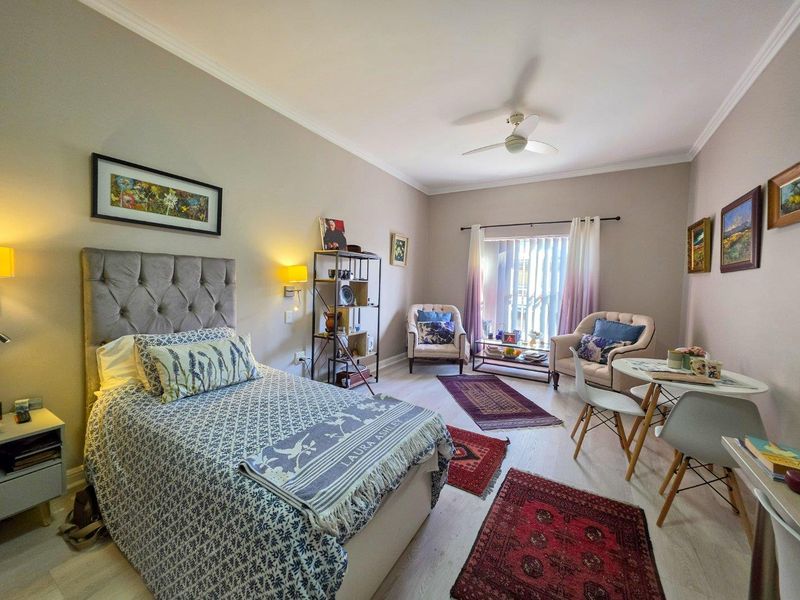 A well-maintained bedroom featuring light laminate flooring, a ceiling fan, and a sliding glass door providing natural light and access to the exterior.