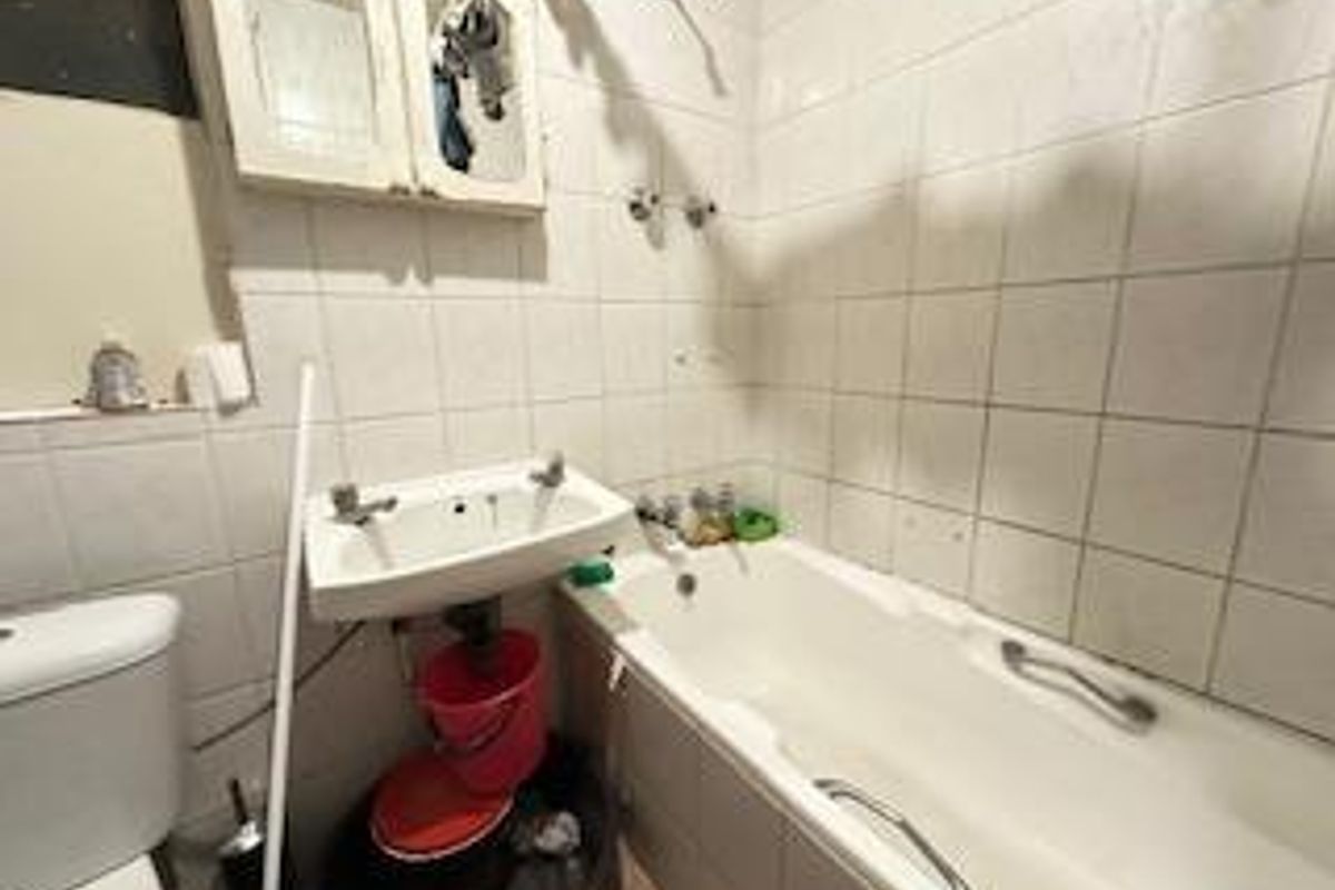 A dated bathroom featuring a standard bathtub, wall-mounted basin, and tiled walls, requiring cosmetic updates to modernize the space.