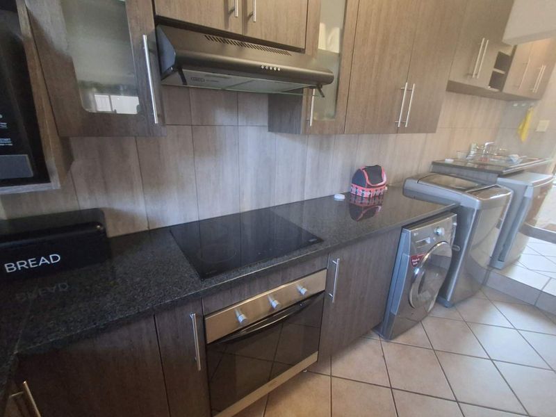 A functional kitchen featuring dark wood cabinetry, granite countertops, a built-in oven with electric hob, and integrated laundry appliance space.
