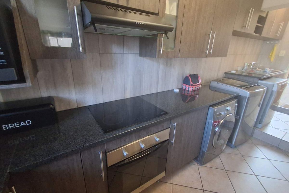 A functional kitchen featuring dark wood cabinetry, granite countertops, a built-in oven with electric hob, and integrated laundry appliance space.