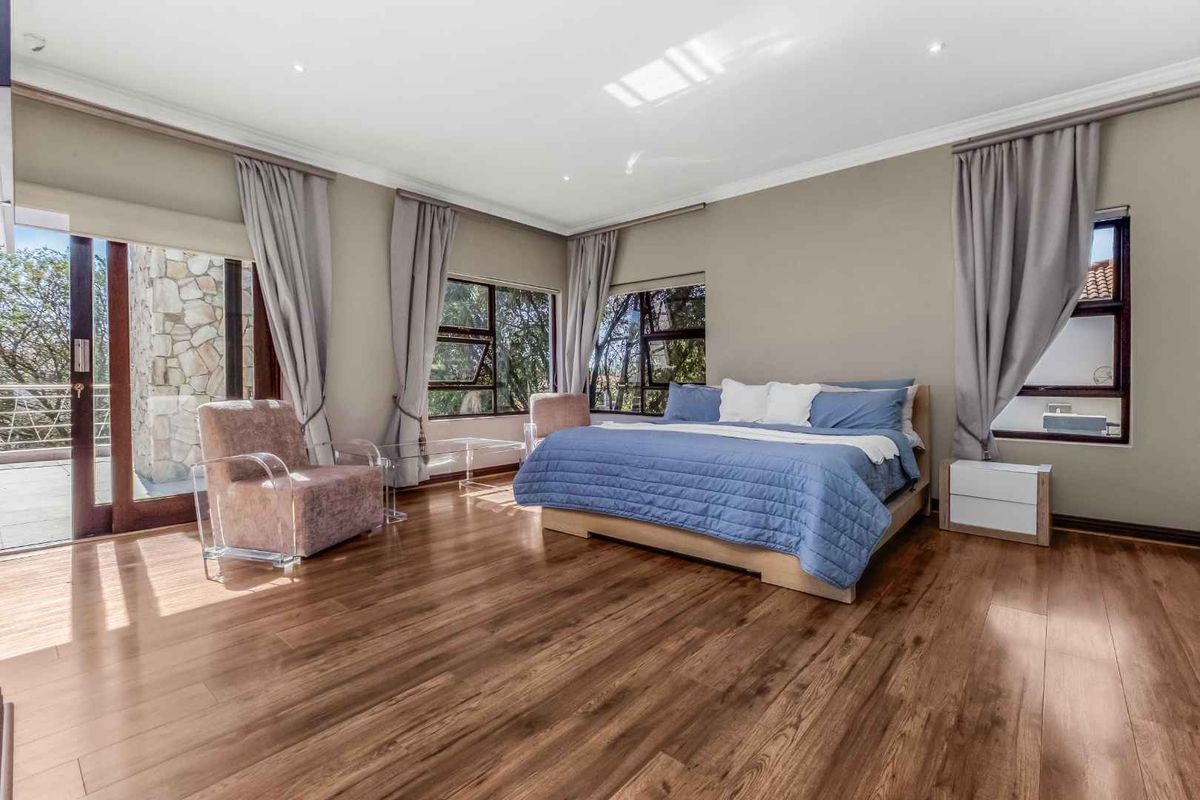 Spacious bedroom featuring warm laminate flooring, recessed downlighting, and large windows with access to an outdoor patio area.